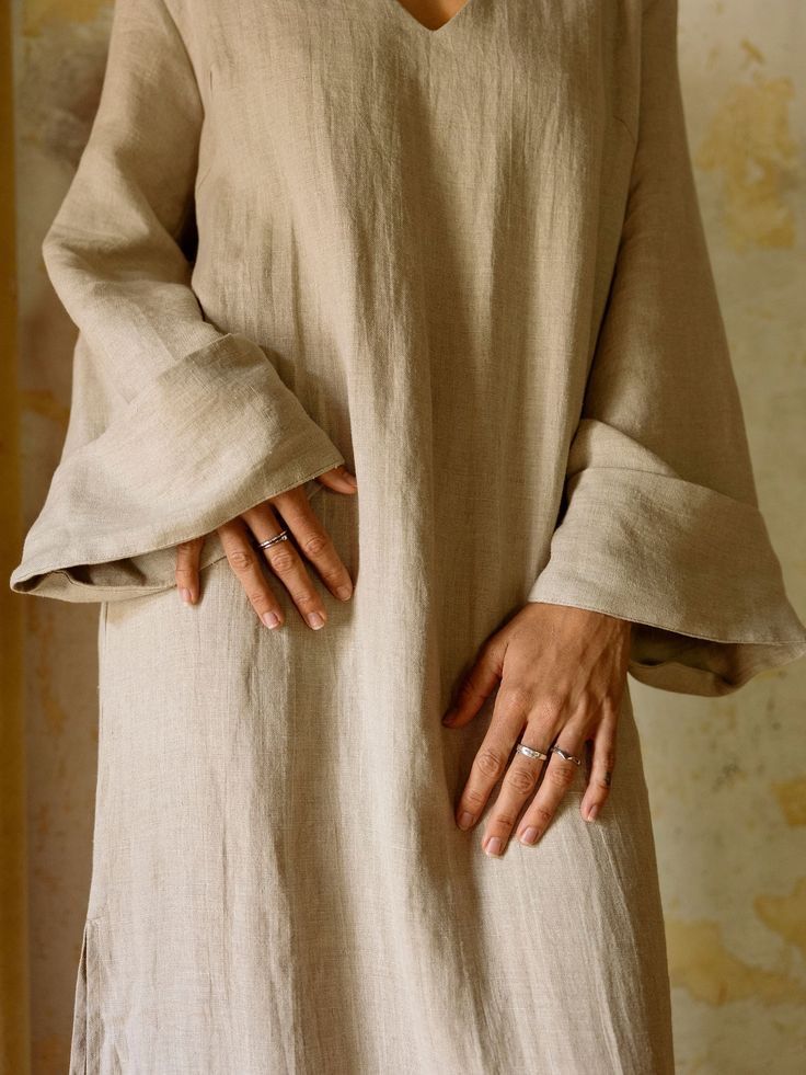 Hands with fine silver rings resting against a loose natural linen dress with deep cuffs