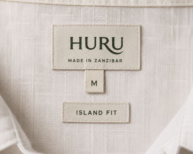 Close-up of a HURU neck label with size M and Island Fit tabs on white linen