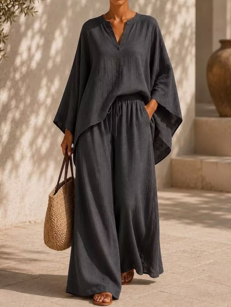 Woman in a charcoal linen set standing on sunlit stone steps, palm shadows moving across a plaster wall