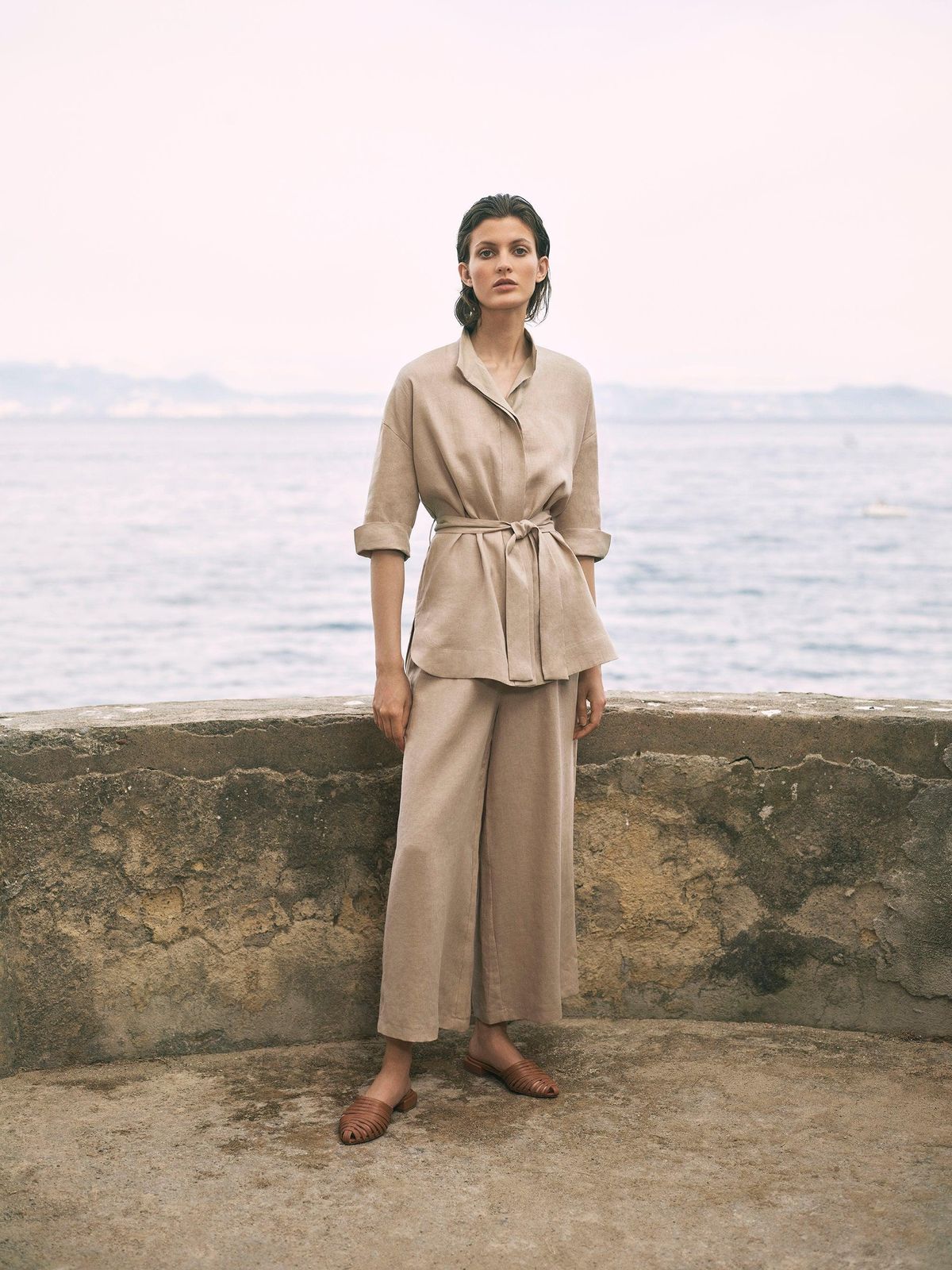 Woman in a sand linen jacket and trousers standing on an old stone sea wall above the Indian Ocean